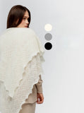 An indoor lifestyle photo featuring the oversized ecru winter wrapping scarf catching a soft breeze against a white background. Macro photography focusing on the fluffy, soft fibers of the cream-white hand-knitted pashmina wrap. The image captures the premium quality and itch-free comfort of the insulating natural down.