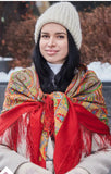 Woman wearing a colorful orange red patterned scarf with silky fringe  and white knit hat in a snowy outdoor setting