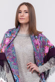 Woman wearing a colorful patterned woolen purple shawl with fringes on a white background