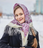 Woman wearing a patterned woolen Slavic scarf white with purple pattern and fringes in a snowy outdoor setting
