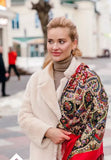 Woman wearing a white coat and colorful patterned red woolen scarf in an urban setting