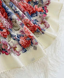Floral patterned merino wool white shawl with colorful pink and blue flowers and fringe on a white background