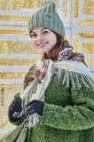Woman wearing a green knit hat, scarf, and gloves against a decorative background.
