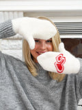 Cozy 80 percent wool mittens for women designed to provide heavy-duty insulation and wind protection during freezing cold weather. A smiling woman posing in front of a fireplace while wearing soft, fluffy white handwarmers with extended elastic ribbed wrist cuffs.