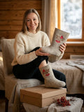 Slavic woman seating on a chair covered with linen fabric and wearing felted boots in traditional Slavic style with rowan berry embroidery and natural wool.