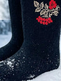 Studio product graphic showcasing a pair of authentic black wool felt winter boots placed on clean white snow against a blurred winter forest background. The image includes text overlays in white stating "100% sheep wool" with a yarn icon, and "warmth and comfort down to minus 35 degrees Celsius" with a snowflake emblem. The boots display an ornate Slavic folklore-inspired red berry branch embroidery stitched onto the wide-cut shaft.