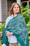 Woman wearing a teal patterned woolen shawl outdoors with greenery in the background