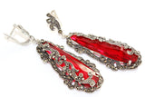Oversized Tudor-style ring and long drop earrings set in bright, shiny 925 silver. The intense red color of the translucent faceted stones beautifully complements the dark, metallic shimmer of the surrounding marcasites. Every element reflects a rich, luxurious look with deep cultural roots.