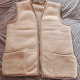 A beige sherpa fleece zip-up vest laid flat on a gray and white striped quilted bedspread.