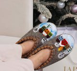 Gray chunky woolen slippers with winter-themed designs worn by a person, with a Christmas tree in the background.