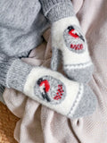 Grey and white wool mittens featuring a circular knit patch with a red bullfinch bird and rowan berries. The thick woven cuffs match the grey sweater sleeve for a seamless winter style look.