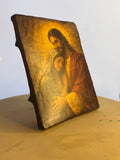 Intimate Christian artwork showing Jesus blessing the Blessed Mother in a warm golden glow. Close-up of a rustic wood block icon featuring Christ and Mary with gold leaf details.