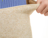 A close-up of a person wearing a blue ribbed sweater and pulling a beige elastic waist fur warmer or belly band outward with their hand.