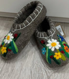 Pair of gray slippers with floral designs on a wooden floor.