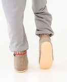 Person wearing gray pants with beige woolen slippers on a white background