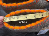 Gray felted slippers with orange stitching being measured with a tape measure.