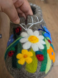 Handmade felted ball with floral and ladybug designs on a wooden surface