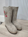 Wide shaft handwoven valenki in gray melange with red embroidery of rowanberry on a wooden table.