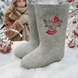 A pair of traditional light gray Slavic valenki felt boots neatly arranged inside a plain brown cardboard shipping box. The boot standing upright showcases beautiful, detailed embroidery on the upper shaft, featuring a vibrant red guelder-rose berry branch with green leaves and brown vine flourishes. The entire boot, from the tall shaft to the rounded toe and bottom sole, is seamlessly crafted from a single piece of thick, natural sheep wool felt without any rubber outsoles