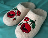 Stylish and therapeutic wool house shoes shaped perfectly for the left and right feet. The light oatmeal-white felted fabric is decorated with intricate folk-art embroidery depicting deep red blooming poppy petals and detailed green foliage.