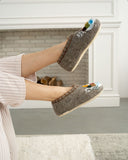 Person wearing brown slippers with colorful designs, standing in a room with a fireplace.