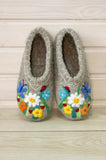 Pair of gray slip on house shoes - slippers made of wool with floral designs on a wooden surface