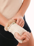 A close-up of a person wearing a beige woolen wrist brace with a fluffy cream natural merino wool fur cuff, shown against a white background.