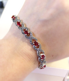A wrist showing a narrow bracelet made of silver and red stones, also shiny marcasite.