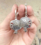 A pair of silver pomegranate earrings with red garnet centers, held in a person's hand. Armenian jewelry online buy with confidence.
