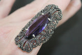 The photo is showcasing a large ring in a shape of peacock tail with marcasite and purple gemstone.