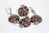 A set of sterling silver jewelry including a pomegranate-shaped earring, ring, and pendant with burgundy red zircon stones.