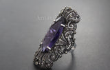 Sterling silver ring featuring a purple lab topaz with intricate designs and marcasite accents on a dark background.